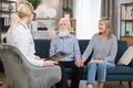 Young high-skilled female healthcare worker, holding CT x-ray scan, consulting joyful senior couple during home visit