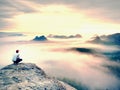 Young hiker in white and black siuts on cliff edge looking to misty hilly valley bellow, fall begins