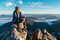 Young hiker woman sitting on the mountain summit cliff, drinking tea from a thermos flask and enjoying mountains valley covered Royalty Free Stock Photo