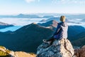 Young hiker woman sitting on the mountain summit cliff and enjoying mountains valley covered with clouds view. Successful summit Royalty Free Stock Photo