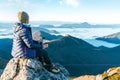 Young hiker woman sitting on the mountain summit cliff and enjoying mountains valley covered with clouds view. Successful summit Royalty Free Stock Photo
