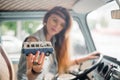 Young hippie woman driving a classic van with a toy car model in her hand. Smiling blurred girl holding a miniature Royalty Free Stock Photo