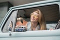 Young hippie woman driving a classic van with a toy car model in her hand. Smiling blurred girl holding a miniature Royalty Free Stock Photo