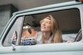 Young hippie woman driving a classic van with a toy car model in her hand. Smiling blurred girl holding a miniature Royalty Free Stock Photo