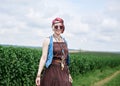 Young hippie woman with short red hair, wearing boho style clothes and sunglasses, dancing on green currant field, posing for Royalty Free Stock Photo