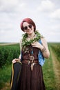 Young hippie woman with short red hair, wearing boho style clothes, sunglasses, with flower wreath on neck, standing on green Royalty Free Stock Photo