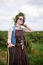 Young hippie woman with short red hair, wearing boho style clothes, sunglasses and flower wreath, standing on green field, holding Royalty Free Stock Photo