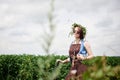 Young hippie woman with short red hair, wearing boho style clothes, sunglasses and flower wreath, standing on green field, holding Royalty Free Stock Photo