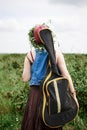 Young hippie woman with short red hair, wearing boho style clothes, sunglasses and flower wreath, walking away from camera on Royalty Free Stock Photo