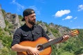 Young hipster bearded guy plays the guitar against the backdrop of a bright summer landscape Royalty Free Stock Photo