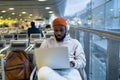 Young hipster black man sitting in airport terminal using laptop wear headphones and listening music Royalty Free Stock Photo