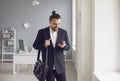Young hipster businessman in black suit reads message in mobile standing in office. Royalty Free Stock Photo