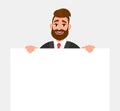 Young hipster businessman showing blank white poster or paper copy space area. Happy trendy person holding empty banner. Royalty Free Stock Photo