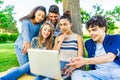 Young hipster friends group sitting on grass in city park making surprise faces looking laptop screen. Modern fun concept with Royalty Free Stock Photo