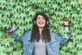Young hipster girl listens to music leaning against an ivy wall - Pretty woman relaxes with headphones in a city park Royalty Free Stock Photo