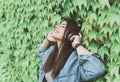 Young hipster girl listens to music leaning against an ivy wall - Pretty woman relaxes with headphones in a city park Royalty Free Stock Photo