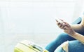 Young hipster girl sitting at airport in yellow boot on suitcase traveling in Europe, female hands using app on making smartphone Royalty Free Stock Photo