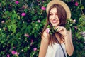 Young hipster girl wearing hat walking by blooming roses. Woman enjoys flowers in park. Summer outfit Royalty Free Stock Photo