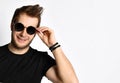 Hipster guy in black t-shirt with print, bracelets. He is smiling and adjusting his sunglasses, posing isolated on white. Close up Royalty Free Stock Photo