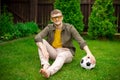 Young hipster guy sits on grass with soccer ball, football fan have leisure time Royalty Free Stock Photo