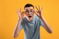 Young hipster guy touching his glasses, opening his mouth in shock on orange studio background Royalty Free Stock Photo