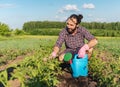 Young hipster male in gloves with a watering can caring for plants potatoes in the garden