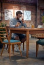 Young hipster man with earphones, siting in cafeteria, drinking coffee. Scrolling through his phone Royalty Free Stock Photo