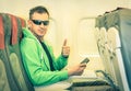 Young hipster man passenger with thumbs up in airplane