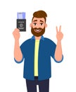 Young hipster man showing passport with tickets and gesturing victory, peace sign. Bearded person holding boarding pass and making