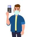 Young hipster man wearing medical mask and showing passport and ticket. Trendy person covering face protection from virus.