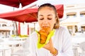 Young hipster millennial cute girl sitting outdoor at bar eating a croissant. Beautiful girl having breakfast in hotel dehors