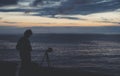 Young hipster relax beach on background ocean sunrise, silhouette romantic person making photo view evening seascape, photographer Royalty Free Stock Photo