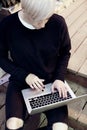 Young hipster woman with blonde short hair sitting on stairs, working on modern laptop computer, look down, touching keyboard