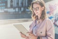 Young hipster woman in glasses stands on city street and uses tablet computer.Girl looking on screen of digital tablet. Royalty Free Stock Photo