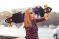 Young hipster woman holding skateboard behind head in sunset, outdoors, cinematic style. Stylish lucky hipster woman Royalty Free Stock Photo