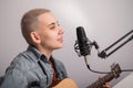 Young hipster woman is recording a song at home recording studio. The girl plays an acoustic guitar and sings into a Royalty Free Stock Photo