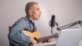 Young hipster woman is recording a song at home recording studio. A girl plays an acoustic guitar sings into a Royalty Free Stock Photo