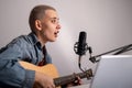 Young hipster woman is recording a song at home recording studio. A girl plays an acoustic guitar sings into a Royalty Free Stock Photo