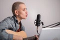 Young hipster woman is recording a song at home recording studio. A girl plays an acoustic guitar sings into a Royalty Free Stock Photo