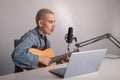 Young hipster woman is recording a song at home recording studio. A girl plays an acoustic guitar sings into a Royalty Free Stock Photo