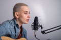 Young hipster woman is recording a song at home recording studio. The girl plays an acoustic guitar and sings into a Royalty Free Stock Photo