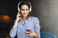 Young hipster woman in room and enjoying music streamed from mobile phone. Girl in earphones listening to songs from playlist in Royalty Free Stock Photo