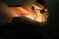 Young hipster woman in santa hat opening magical present in dark room and smiling. Merry Christmas. Stylish happy girl in cozy Royalty Free Stock Photo