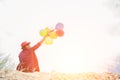 Young hipster woman sitting on the sand and holding colorful balloons