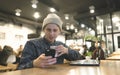 A young hipsters stares at his own snapphone and drinks coffee while working on a laptop in a cafe. Royalty Free Stock Photo