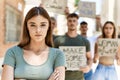 Young hispanic activist woman with arms crossed gesture standing with a group of protesters holding banner protesting at the city Royalty Free Stock Photo