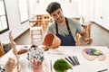 Young hispanic artist man smiling happy painting pottery at art studio