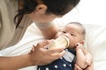 Young hispanic baby or asian infant boy drinking milk from plastic bottle feeding from young parents mother or babysitter