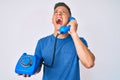 Young hispanic boy holding vintage telephone angry and mad screaming frustrated and furious, shouting with anger looking up Royalty Free Stock Photo