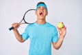 Young hispanic boy playing tennis holding racket and ball angry and mad screaming frustrated and furious, shouting with anger Royalty Free Stock Photo